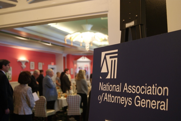 A sign that says National Association of Attorneys General in front of a group of people